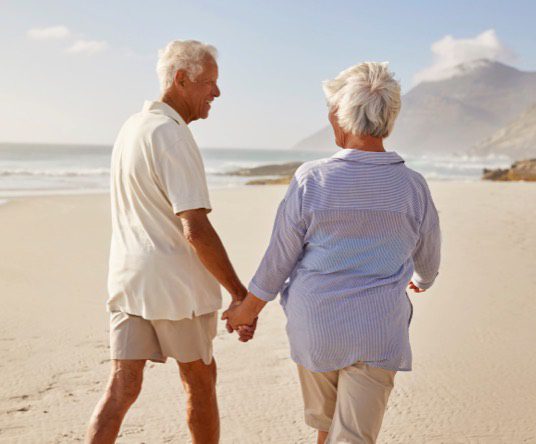 old couple holding hands while walking at the beach